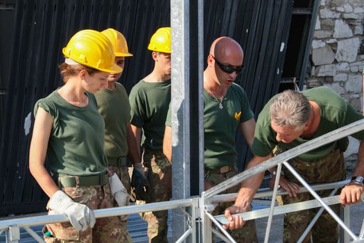 A group of engineers in safety helmets and military uniforms assembling a metal structure with focus.