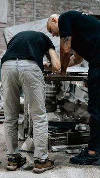 Two workers collaborate intensely at an industrial workbench in a workshop.