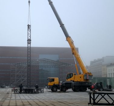 A large crane lifting metal structure in an urban square with foggy backdrop.