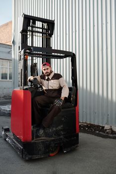 Male forklift operator working outdoors near industrial building.