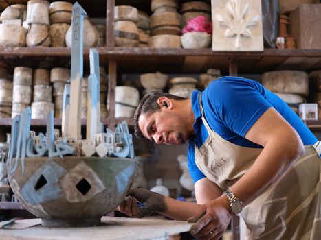 A focused craftsman sculpting detailed artwork in a workshop full of materials and tools.